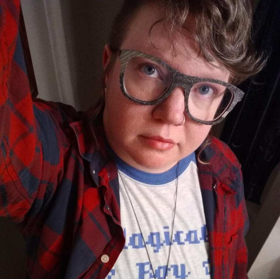 Selfie of genderqueer boy in big glasses and red flannel looking up thoughtfully at the camera.